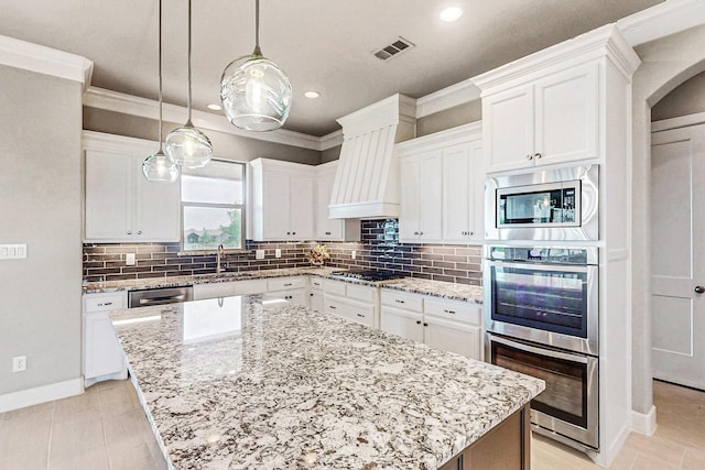 kitchen featuring white cabinets, decorative light fixtures, a kitchen island, and appliances with stainless steel finishes