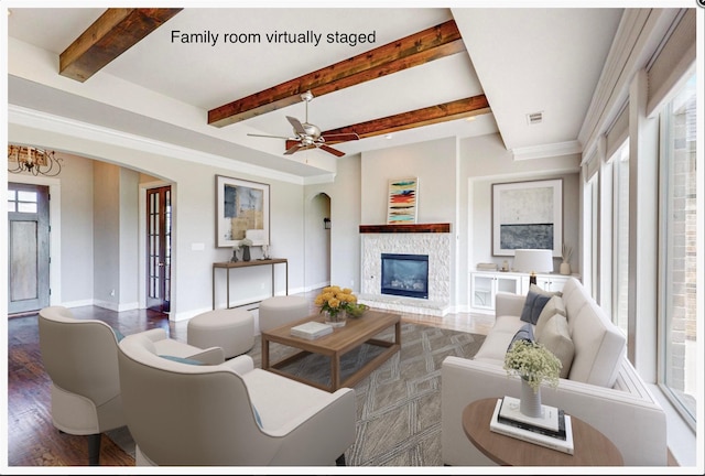 living room with beamed ceiling, dark hardwood / wood-style floors, a stone fireplace, and ceiling fan with notable chandelier