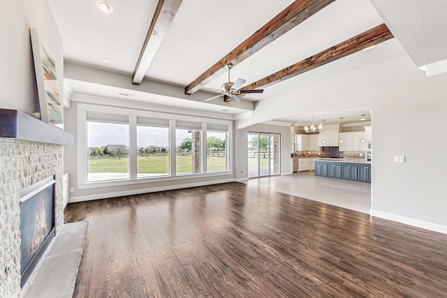 unfurnished living room with a fireplace, beam ceiling, ceiling fan with notable chandelier, and dark wood-type flooring