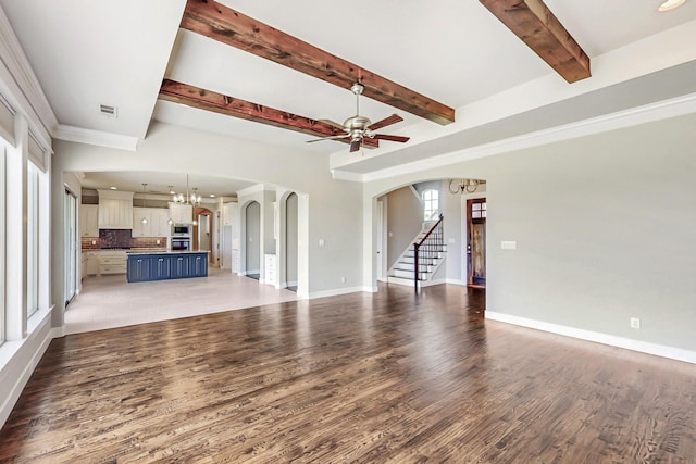 unfurnished living room with beamed ceiling, ceiling fan with notable chandelier, dark hardwood / wood-style floors, and a wealth of natural light