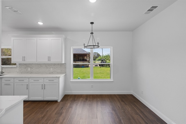 kitchen featuring pendant lighting, backsplash, dark hardwood / wood-style floors, light stone countertops, and white cabinetry