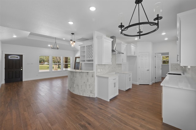 kitchen featuring wall chimney exhaust hood, white cabinetry, backsplash, and an inviting chandelier