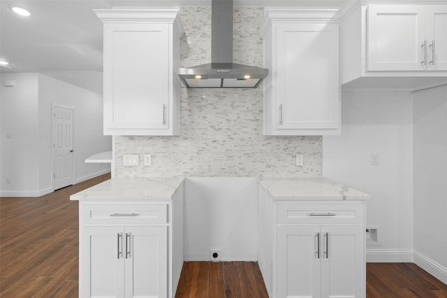 kitchen featuring wall chimney exhaust hood, light stone counters, white cabinetry, and dark wood-type flooring