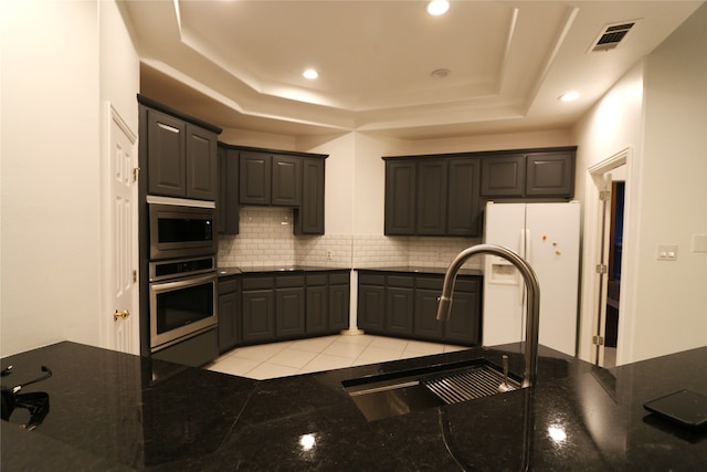 kitchen with light tile flooring, stainless steel appliances, backsplash, a tray ceiling, and sink