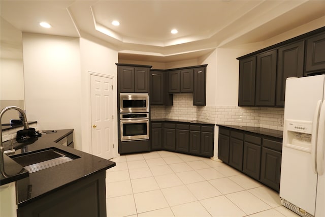 kitchen with appliances with stainless steel finishes, sink, tasteful backsplash, light tile floors, and a raised ceiling