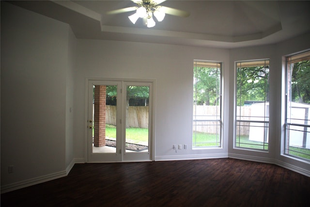 unfurnished room featuring a wealth of natural light, ceiling fan, dark hardwood / wood-style flooring, and a tray ceiling