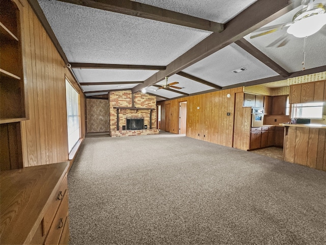 unfurnished living room with a brick fireplace, a textured ceiling, dark colored carpet, vaulted ceiling with beams, and wood walls