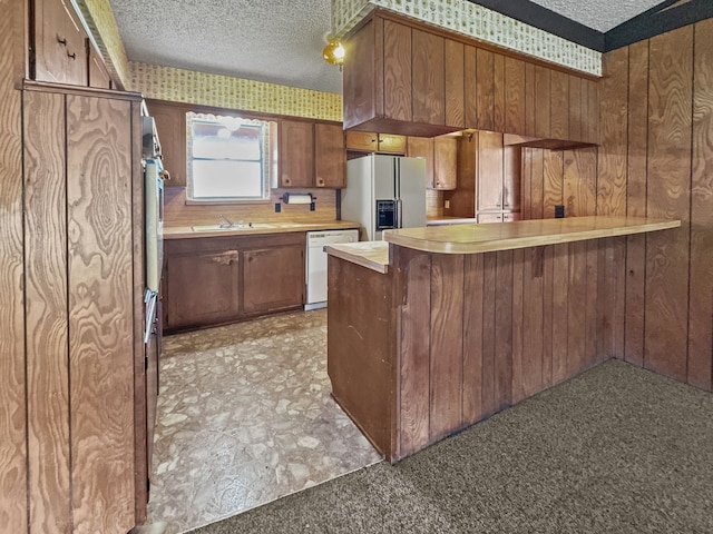 kitchen featuring white appliances, sink, wooden walls, a textured ceiling, and kitchen peninsula