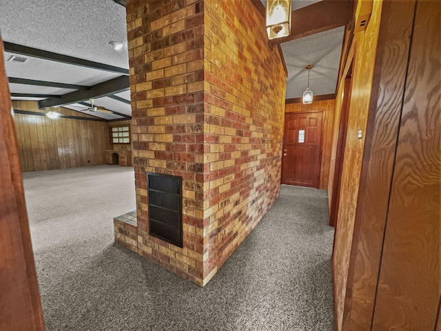 hall featuring dark colored carpet, lofted ceiling with beams, a textured ceiling, and wooden walls