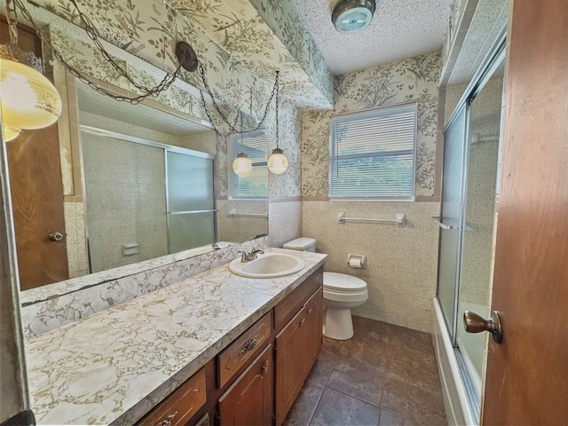 full bathroom with a textured ceiling, toilet, shower / bath combination with glass door, vanity, and tile walls