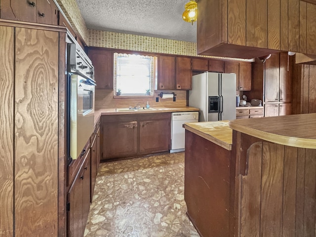 kitchen featuring sink, white appliances, and a textured ceiling