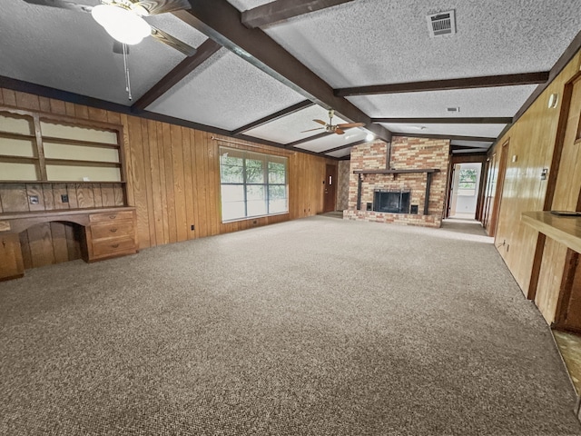 unfurnished living room featuring carpet, a brick fireplace, a textured ceiling, ceiling fan, and vaulted ceiling with beams