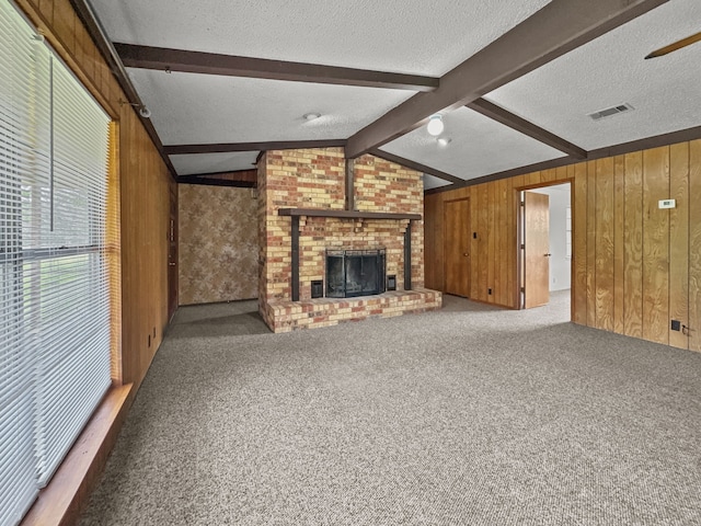 unfurnished living room with lofted ceiling with beams, wooden walls, carpet flooring, a fireplace, and a textured ceiling