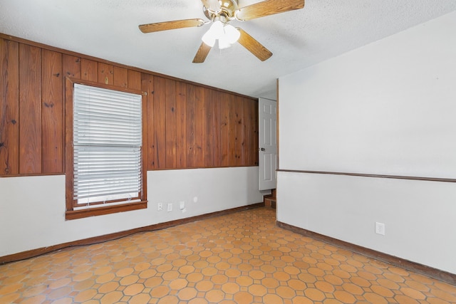 spare room featuring a textured ceiling, ceiling fan, and wood walls