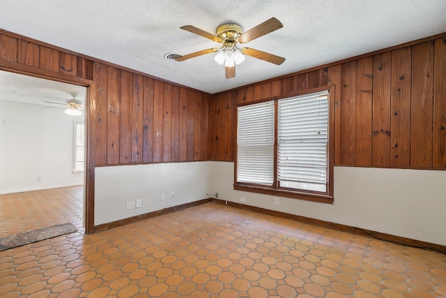 spare room featuring wooden walls, ceiling fan, and a textured ceiling