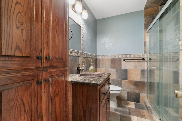 bathroom with vanity, toilet, a shower with door, and tile walls