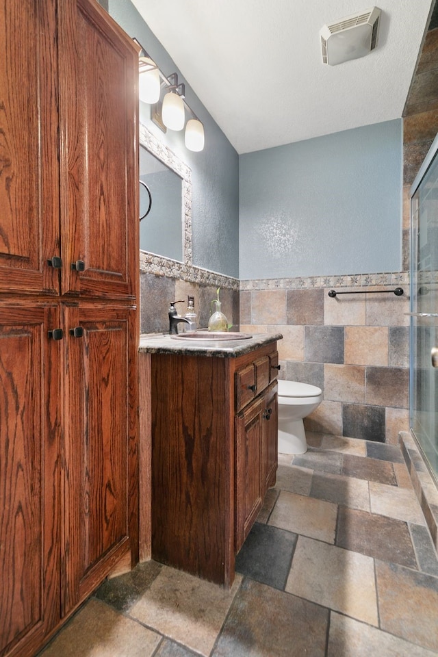 bathroom with vanity, an enclosed shower, tile walls, and toilet