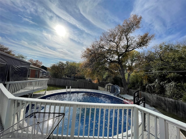 view of swimming pool with a wooden deck, a water slide, and a shed