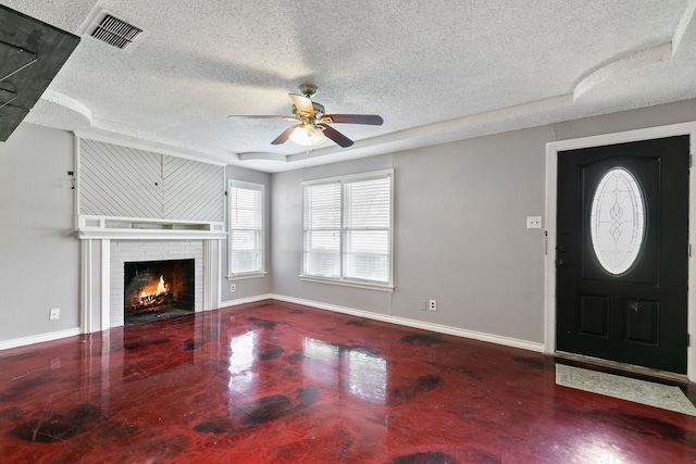 foyer entrance with ceiling fan, concrete flooring, a textured ceiling, and a brick fireplace