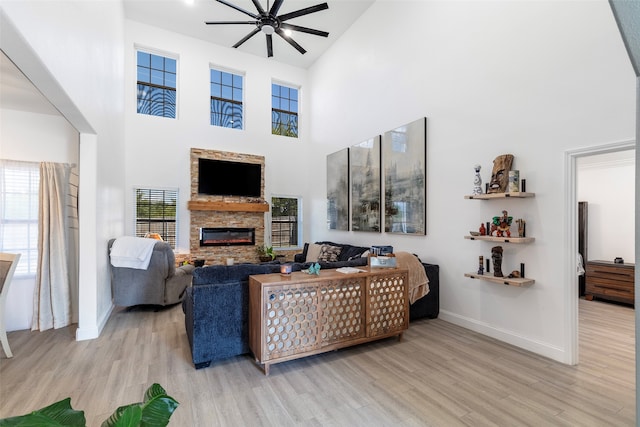 living room featuring a stone fireplace, high vaulted ceiling, ceiling fan, and light hardwood / wood-style flooring