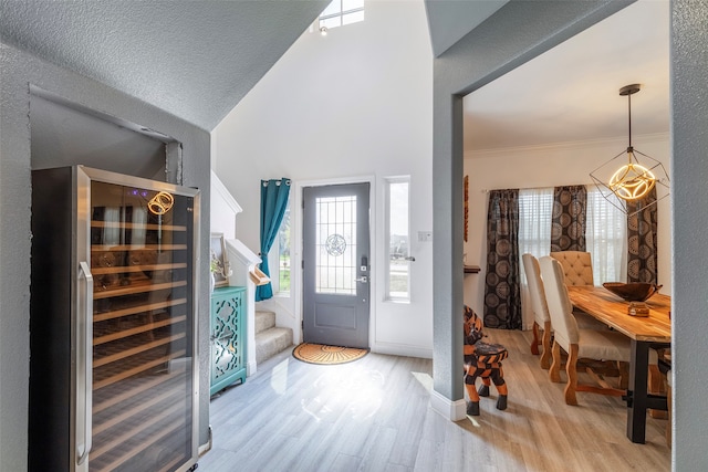 entryway with high vaulted ceiling, beverage cooler, a textured ceiling, and light wood-type flooring