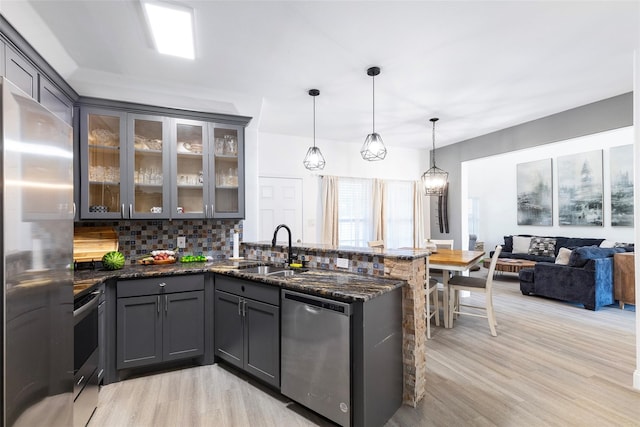 kitchen with light hardwood / wood-style floors, appliances with stainless steel finishes, dark stone counters, decorative light fixtures, and tasteful backsplash