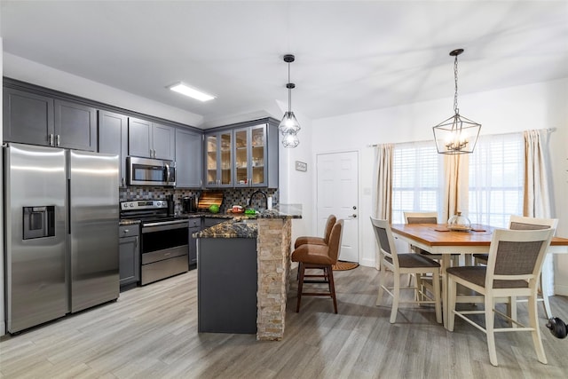 kitchen with decorative light fixtures, light wood-type flooring, backsplash, and appliances with stainless steel finishes