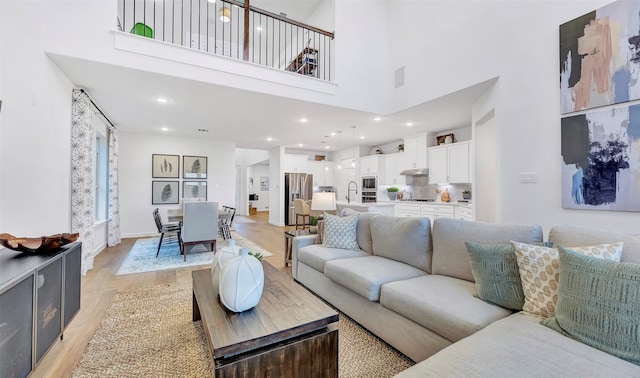 living room featuring a towering ceiling, sink, and light wood-type flooring