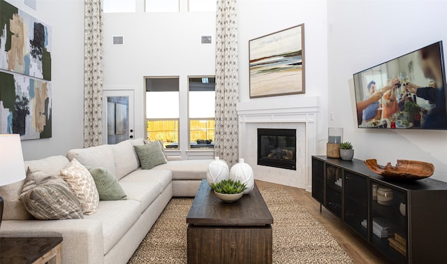 living room featuring a towering ceiling, a tile fireplace, and dark wood-type flooring