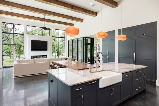 kitchen with pendant lighting, sink, light stone countertops, an island with sink, and a large fireplace