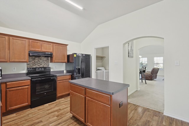 kitchen featuring vaulted ceiling, black appliances, washer and dryer, a center island, and light hardwood / wood-style floors