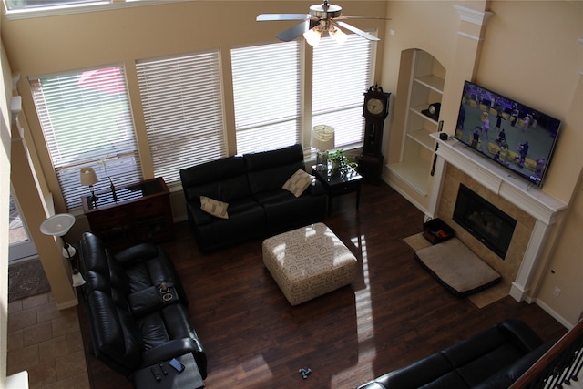 living room with dark hardwood / wood-style flooring, built in shelves, ceiling fan, and a towering ceiling