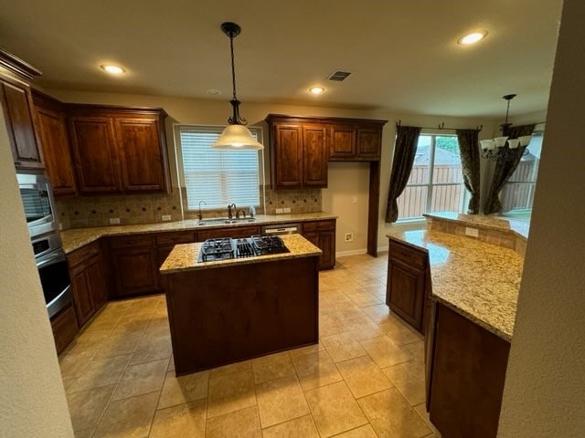 kitchen featuring light stone counters, a kitchen island, sink, decorative backsplash, and black gas cooktop