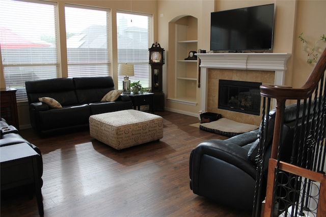 living room featuring built in features, a tiled fireplace, and dark hardwood / wood-style floors