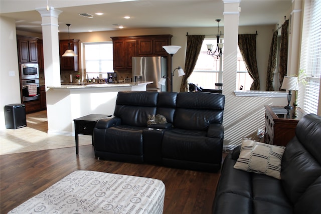 living room with a chandelier, hardwood / wood-style floors, ornate columns, and plenty of natural light