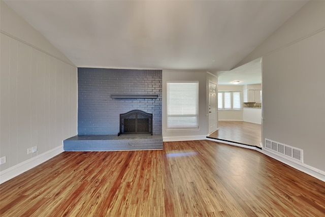 unfurnished living room with a brick fireplace, vaulted ceiling, brick wall, and wood-type flooring