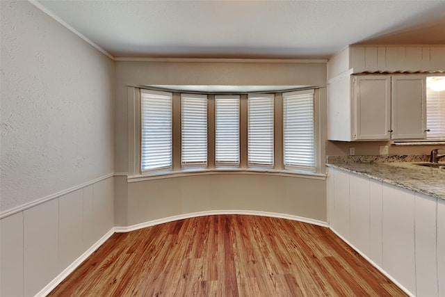 unfurnished dining area featuring crown molding, sink, and light hardwood / wood-style flooring