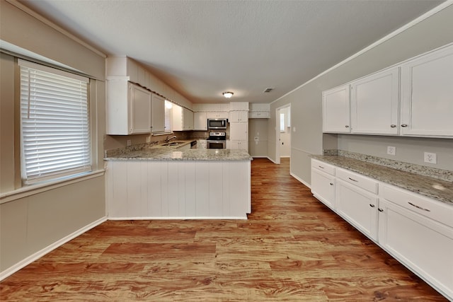 kitchen featuring white cabinetry, wood-type flooring, light stone counters, ornamental molding, and sink