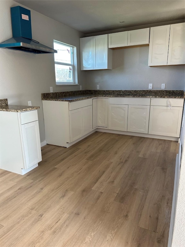 kitchen with light hardwood / wood-style floors, white cabinetry, dark stone counters, and range hood