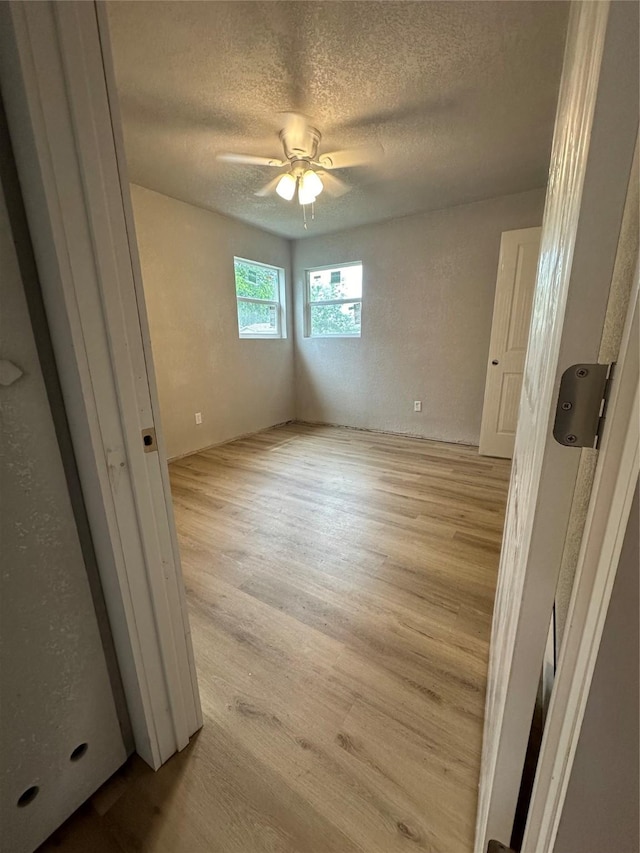 empty room with a textured ceiling, ceiling fan, and light hardwood / wood-style flooring