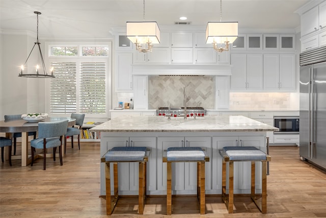 kitchen featuring light wood-type flooring, tasteful backsplash, pendant lighting, and built in appliances