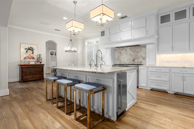 kitchen featuring an island with sink, decorative light fixtures, tasteful backsplash, and light hardwood / wood-style flooring