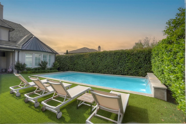 pool at dusk featuring pool water feature and a lawn