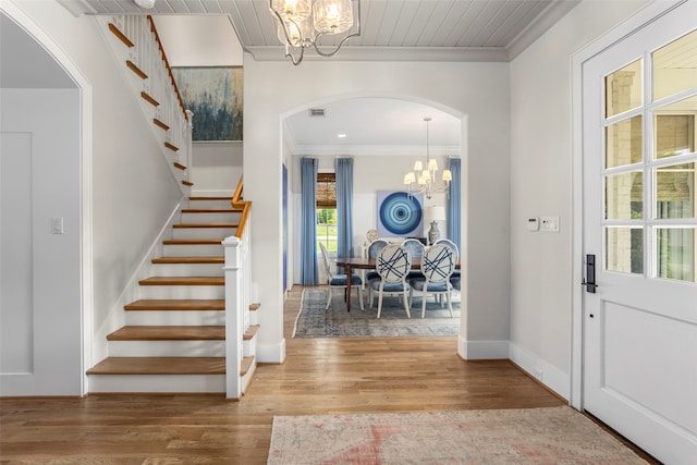 foyer entrance with crown molding, wood-type flooring, and a notable chandelier