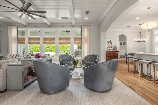 living room featuring beamed ceiling, ornamental molding, light wood-type flooring, and ceiling fan with notable chandelier