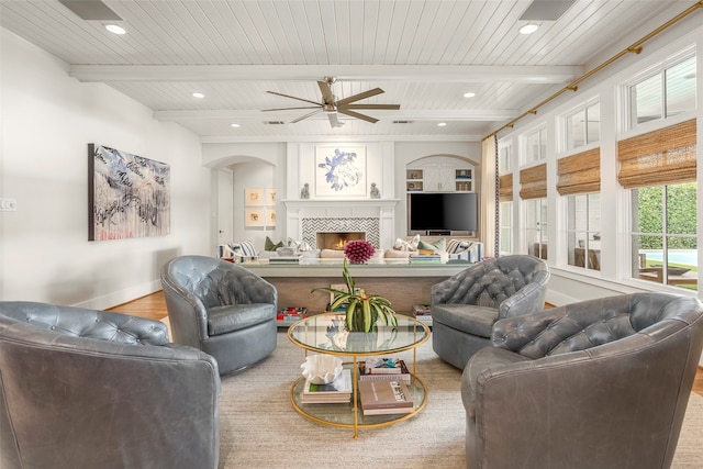 living room with ceiling fan, beam ceiling, wood ceiling, wood-type flooring, and a tile fireplace