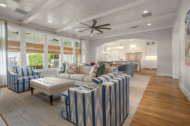 living room featuring beamed ceiling, light hardwood / wood-style floors, a fireplace, and ceiling fan