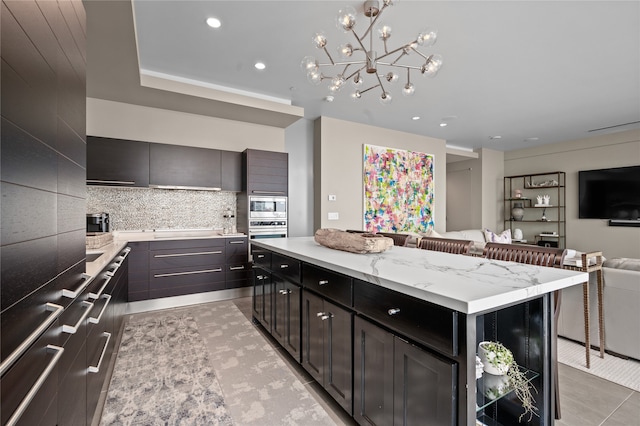 kitchen with a kitchen island, an inviting chandelier, tasteful backsplash, stainless steel oven, and light tile floors