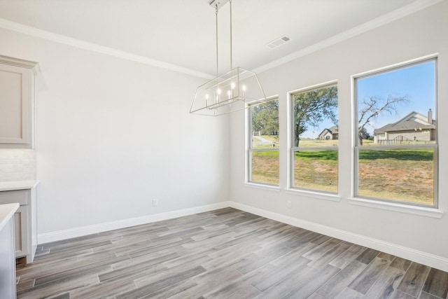 unfurnished dining area with a chandelier, ornamental molding, and light hardwood / wood-style floors