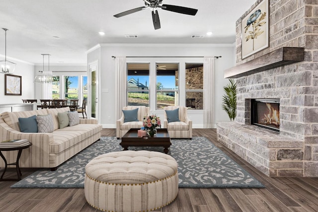 living room featuring dark wood-type flooring, ceiling fan with notable chandelier, and a stone fireplace